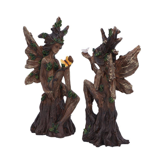 Two carved tree fairy sculptures sit on root-like bases; one cradles a yellow butterfly while the other lifts an arm with a small white bird, photographed on a white background.