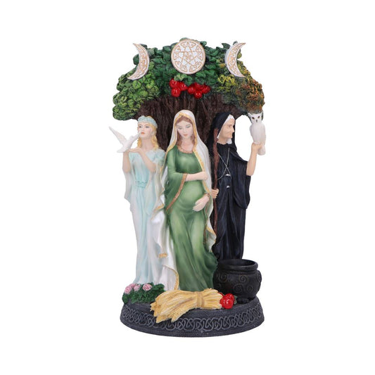 A triple goddess figurine shows three women with a tree overhead, each holding symbolic objects like a dove and owl, sitting atop a decorative base alongside a cauldron.