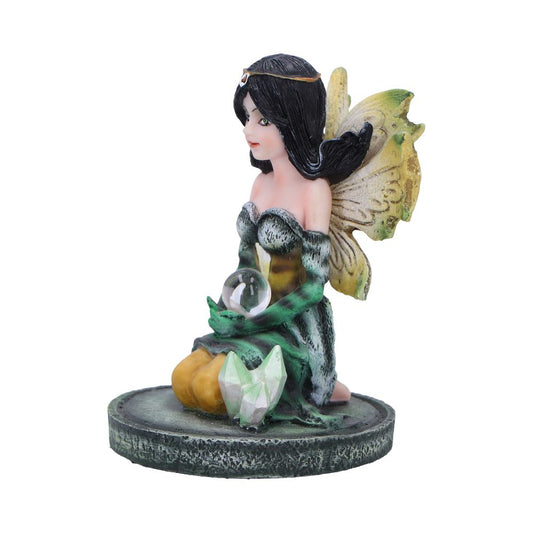 A fairy figurine, seated and holding a crystal ball, rests on a circular base. She wears a green and gold dress with wings. Crystals are at her feet.