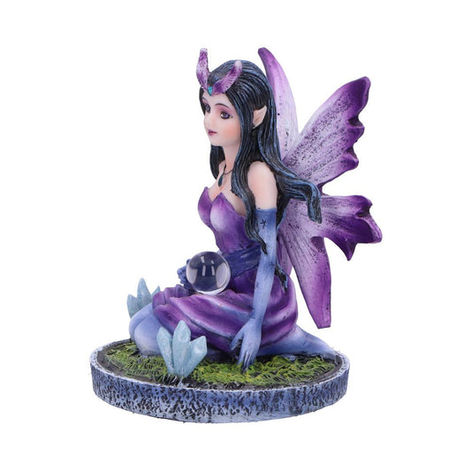 A purple fairy figurine sits on a circular base, holding a crystal ball. She is adorned with wings and wears a flowing gown. The base suggests a grassy, mystical setting.