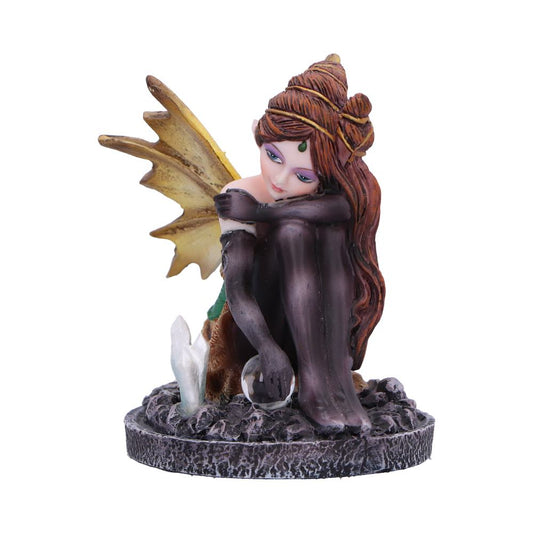 A fairy figurine sits pensively, holding a crystal orb, amidst dark rocks and crystals on a circular base.