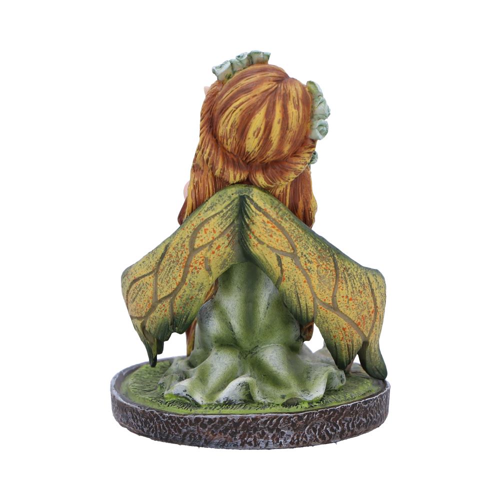 A fairy figurine, seated with leaf-shaped wings, rests on a circular base; it is depicted in a garden setting.