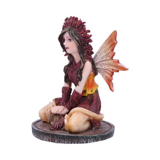 A fairy figurine sits on a base, holding a small orb. The fairy wears autumnal-colored clothing and has large wings. It is displayed against a white background.
