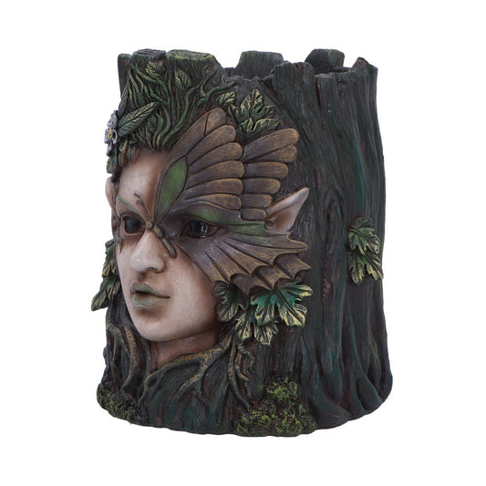 A decorative sculpture depicting a mystical face with pointed ears and a leaf-like mask, emerging from a tree trunk adorned with foliage. The setting is natural and fantastical.