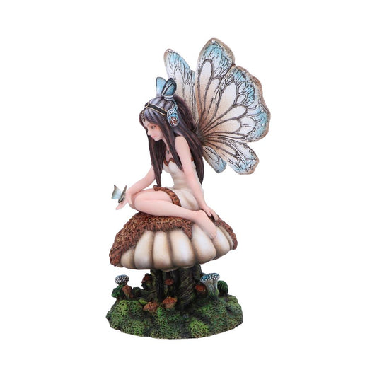 A fairy figurine with delicate wings sits atop a large mushroom, holding a small bird. The scene is set on a green, textured base resembling a forest floor.