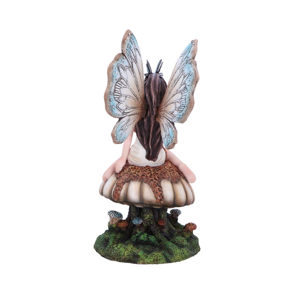 A fairy figurine sits on a large mushroom, wings outstretched. It has long hair, delicate features, and is surrounded by smaller mushrooms on a grassy base.