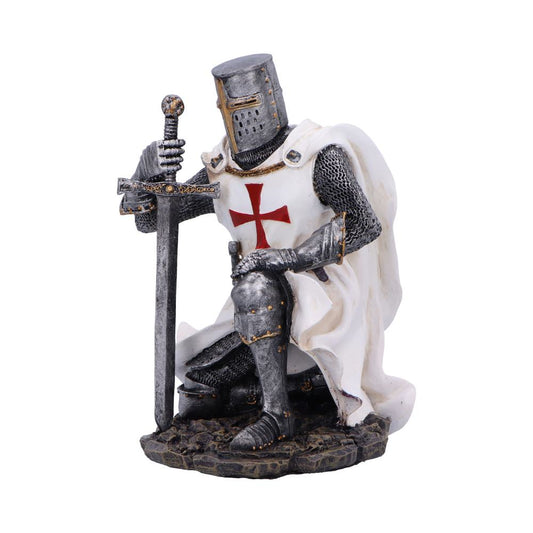 Armored knight figurine kneeling, hands clasping a sword planted point-first, wearing chainmail and white surcoat with red cross, helmeted and draped in cloak on rocky base against white background.
