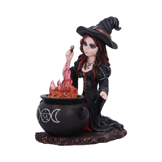 A witch figurine holds a small stone above a cauldron while kneeling; orange translucent flames rise from the cauldron decorated with triple moon and pentagram symbols against a white background.