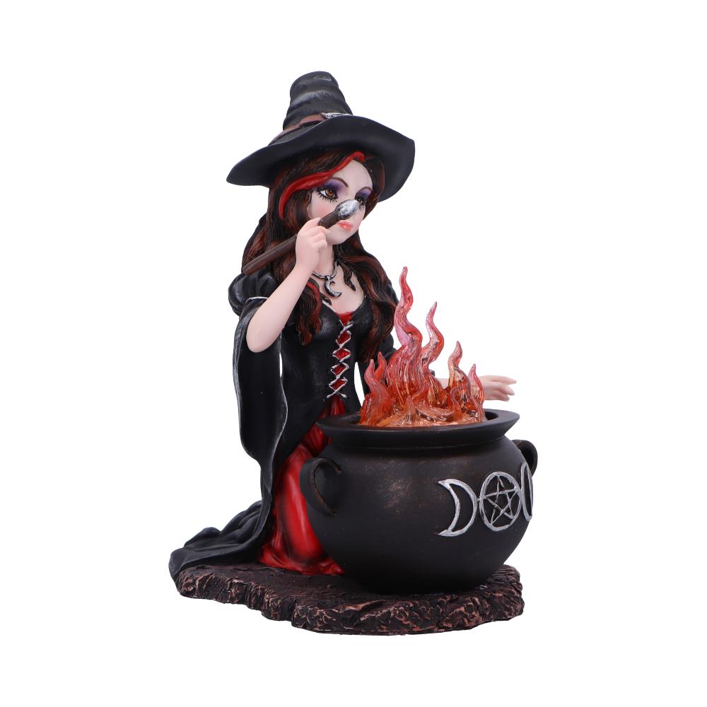 A red-haired witch figurine stirs a bubbling cauldron with flaming orange translucent flames while kneeling on a textured base, wearing a black hat and red-and-black gown.