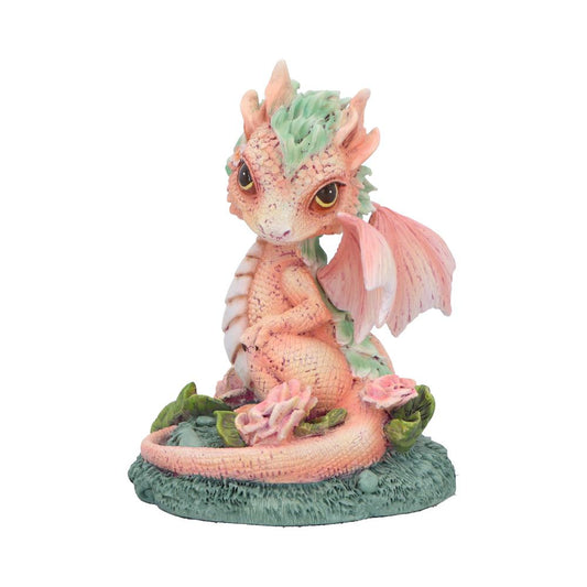 Small pastel pink-green baby dragon figurine sits with curled tail and folded wing, gazing upward from a textured green base adorned with leaves and pink flowers on a white background.