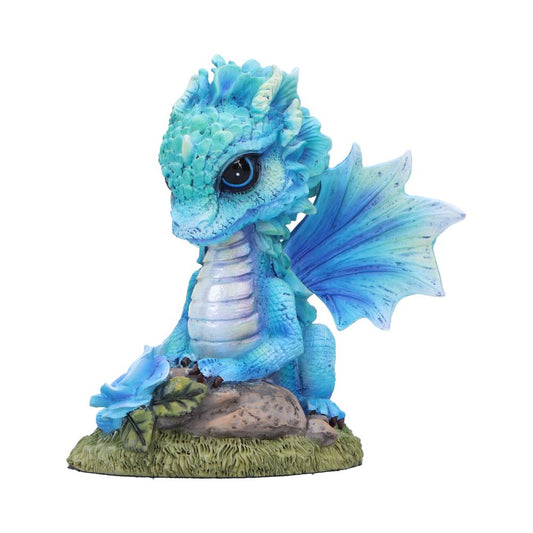 Small blue dragon figurine sits upright, gazing with large eyes, one wing flared while a blue flower rests by its claws on a grassy rock base against a white background.