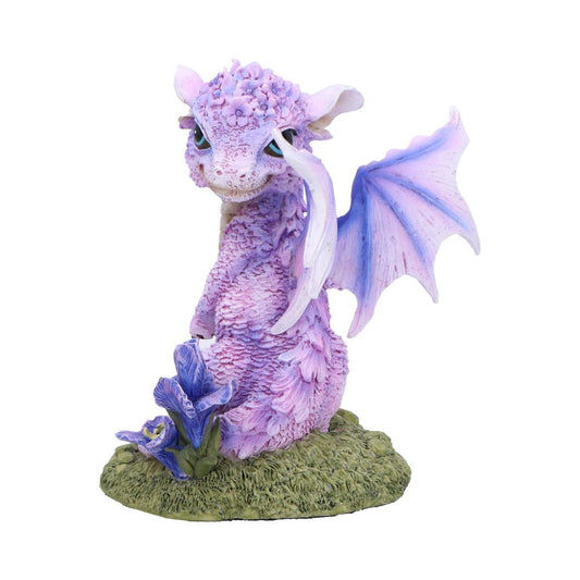 Purple baby dragon figurine tilting its head and lifting a wing, perched on a textured grassy base beside purple flowers against a plain white background.