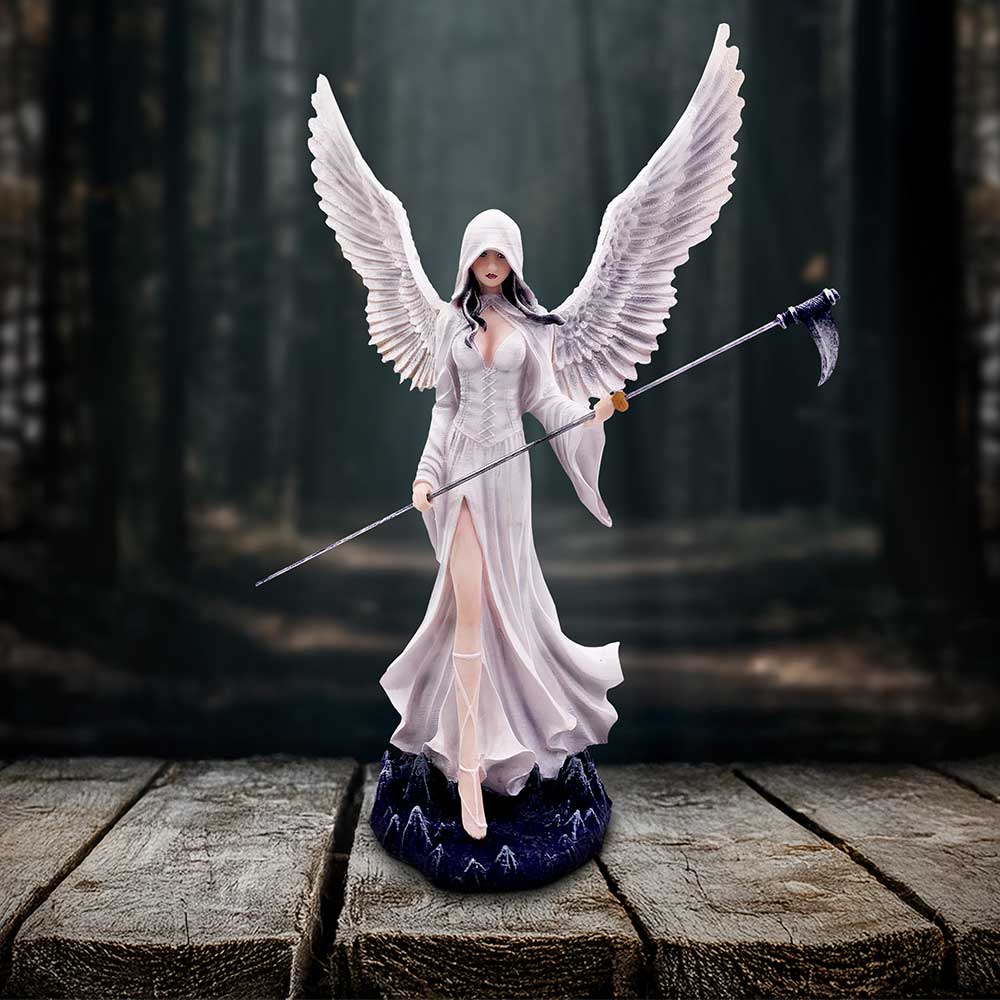 Hooded winged female figurine stands on a rocky base holding a long scythe with wings spread wide while posed on rough wooden planks before a misty dark forest.
