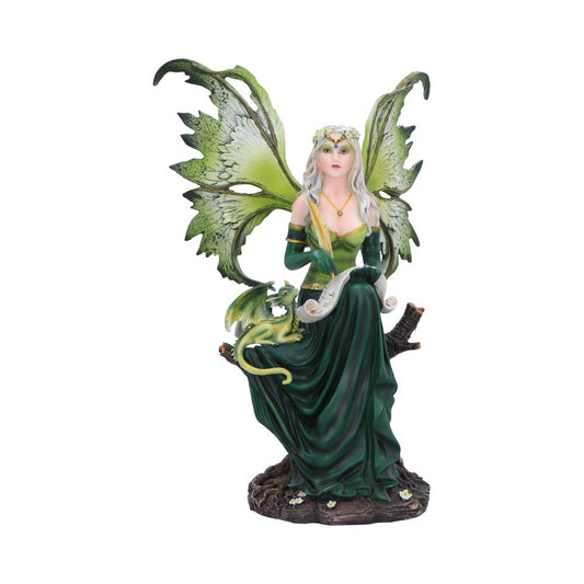 Green-winged fairy statue sits on a tree stump holding a scroll as a small dragon curls on her lap, wearing a flowing green gown and floral crown against white background.