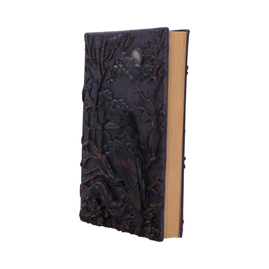 A dark decorative book displays a sculpted raven perched among twisted branches under a moonlit cloudy sky against a white background.