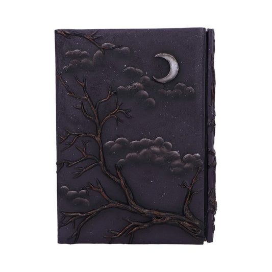 Leather-bound journal depicts a crescent moon and clouds while gnarled bare tree branches climb across its embossed dark cover, photographed isolated against a plain white background.