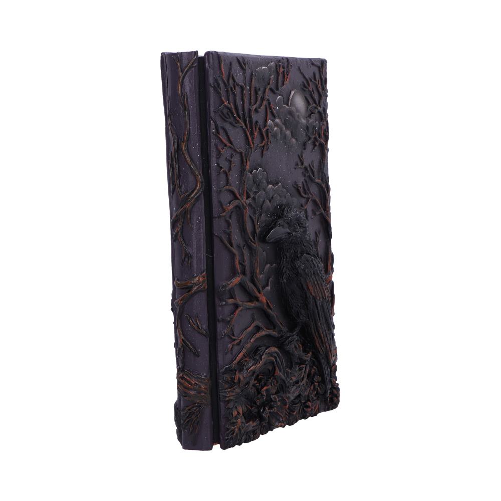 Ornate dark purple journal with a raised raven perched among twisted branches embossed on the cover, standing upright against a plain white studio background.
