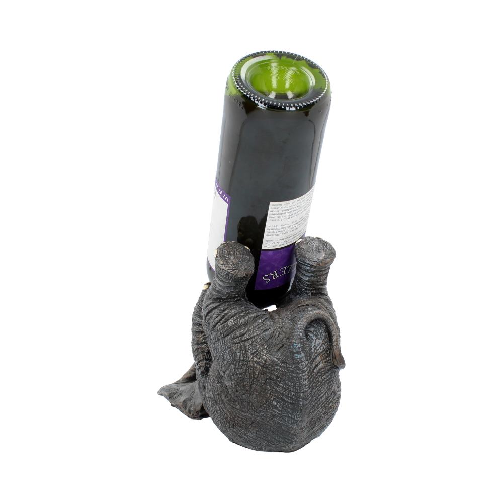 A carved elephant sculpture holds an inverted wine bottle vertically. The bottle's label is visible, featuring purple and white colors. The elephant's textured trunk and legs provide support on a plain background.