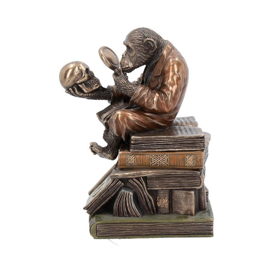 A bronze chimpanzee, wearing a suit, sits atop a stack of books. It holds a human skull in one hand and examines it with a magnifying glass.