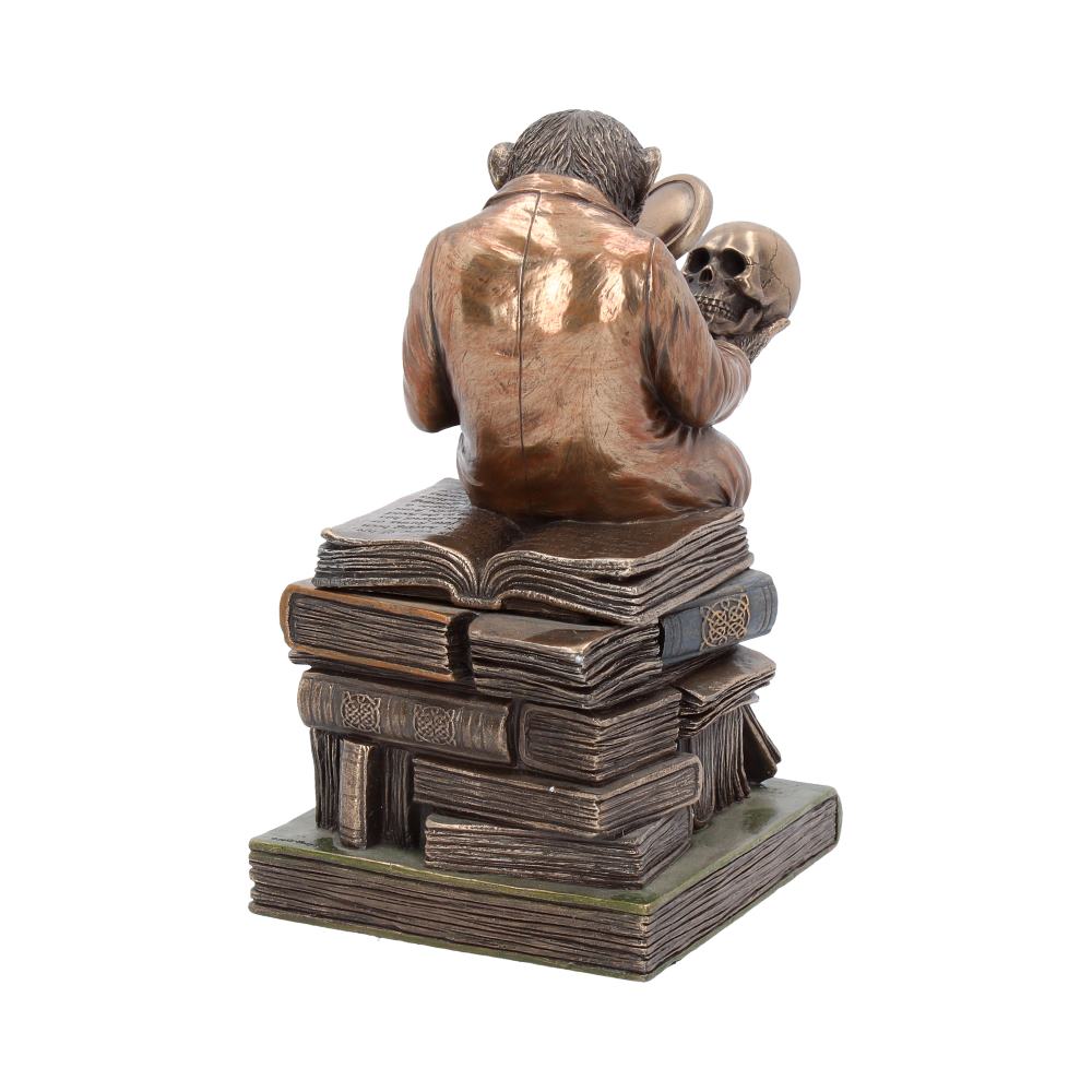 A bronze monkey in a suit sits atop a stack of books, examining a skull with a magnifying glass. The scene is set against a white background.