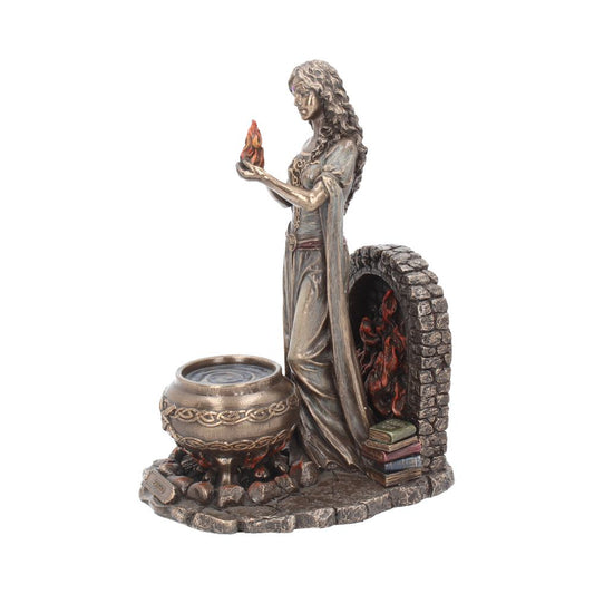 A bronze-colored figurine depicting a woman holding a flame stands beside a cauldron on a rocky base. Behind her, a stone arch shelters books and a small creature.