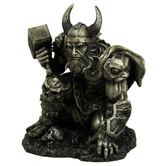 A silver-toned warrior statue crouches, gripping a hammer, in battle armor with horned helmet and animal-themed details, set on a textured rocky base with skulls.