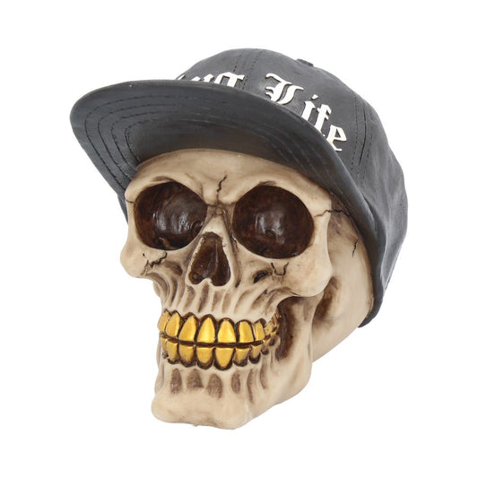 A skull with gold teeth wears a black baseball cap featuring the text "Thug Life," set against a plain white background.