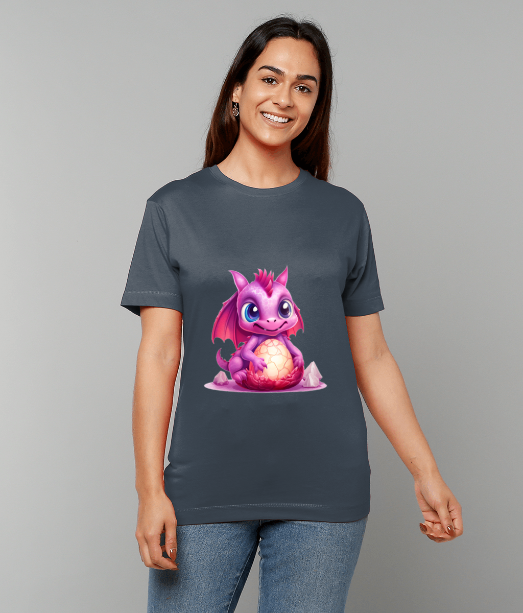 Pink baby dragon sits cradling a glowing cracked egg, printed on a dark gray t-shirt worn by a smiling woman standing against a plain light gray background.