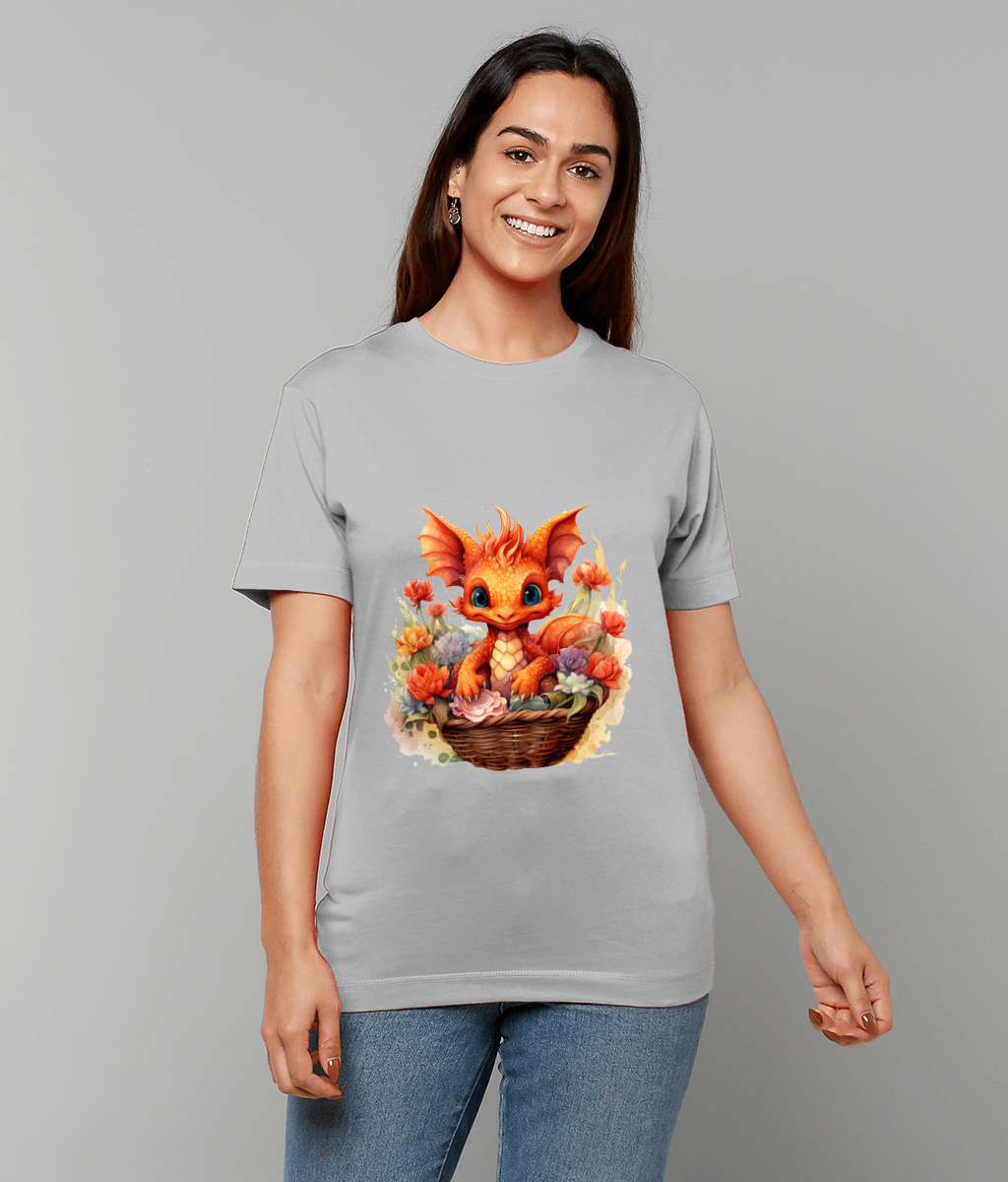 Cartoon orange dragon sits in a woven basket surrounded by colorful flowers printed on a light gray T-shirt worn by a smiling woman standing against a plain pale gray background