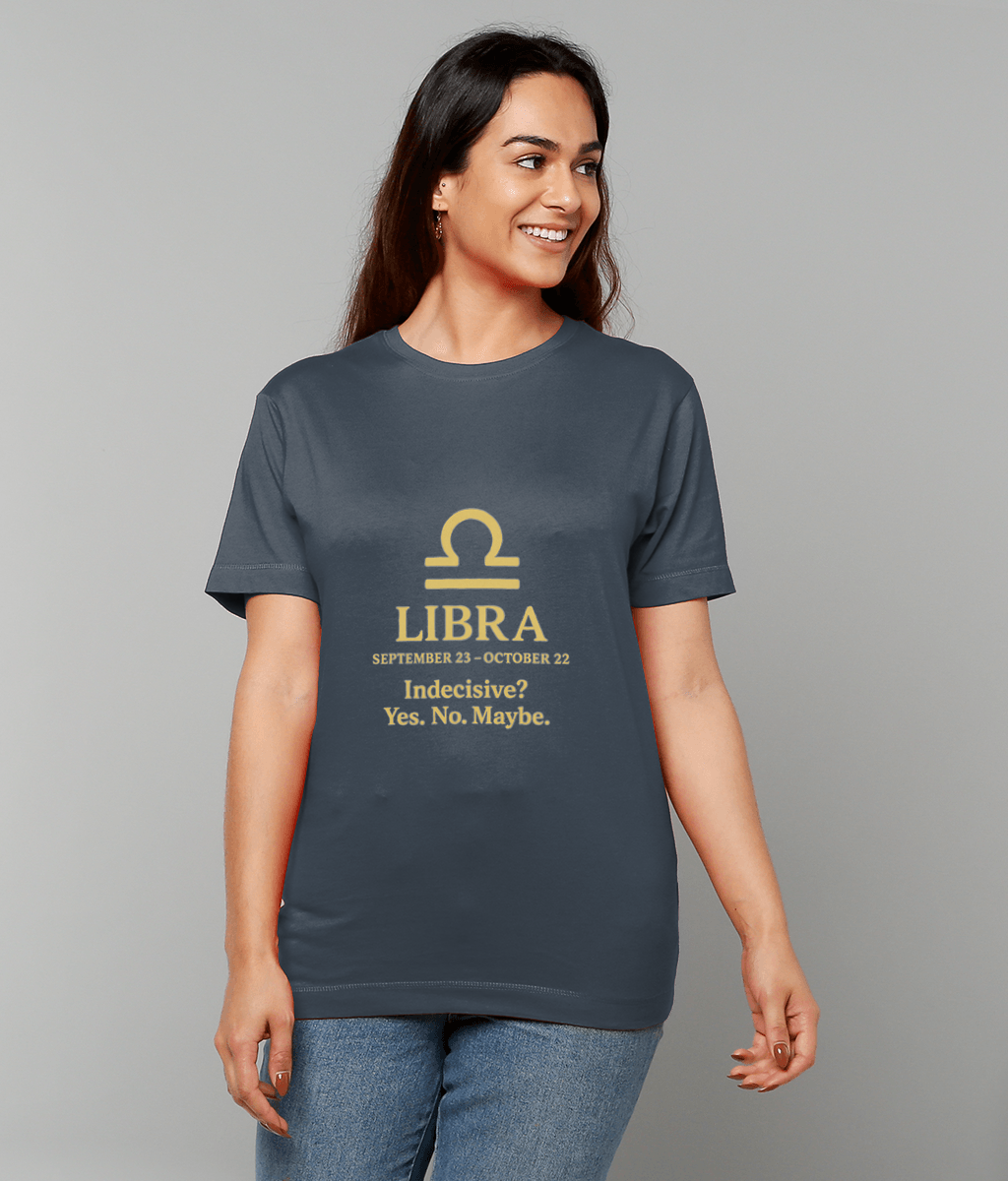 Smiling woman wearing a dark blue T-shirt displaying a yellow Libra symbol above text: "LIBRA SEPTEMBER 23 - OCTOBER 22 Indecisive? Yes. No. Maybe." standing against a plain light gray background