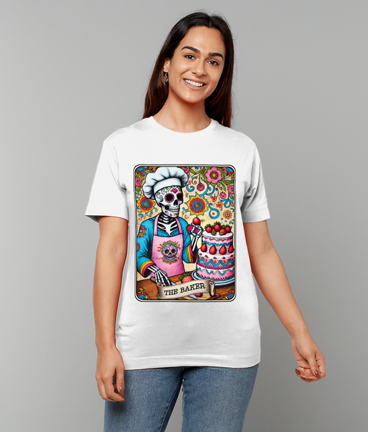 White t-shirt displays a colorful Day of the Dead style skeleton baker decorating a strawberry-topped cake against a floral background; text on design reads THE BAKER.