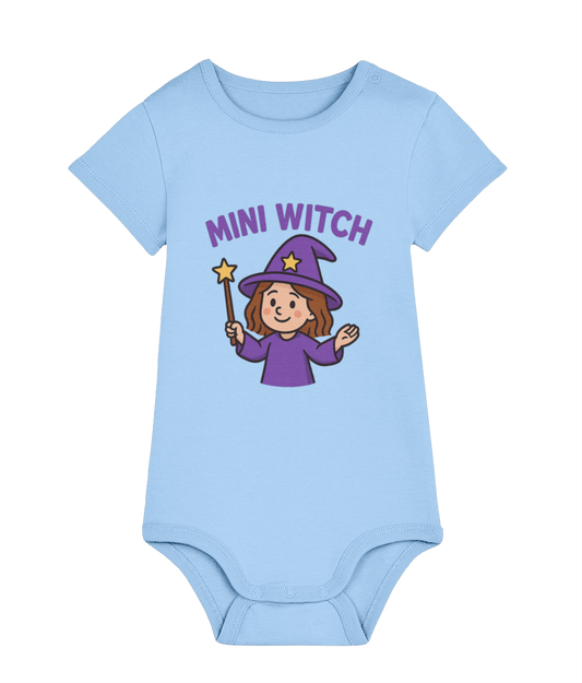 Light blue baby onesie displays a smiling cartoon girl in a purple witch hat waving a star-tipped wand against a black background, text above reads "MINI WITCH".