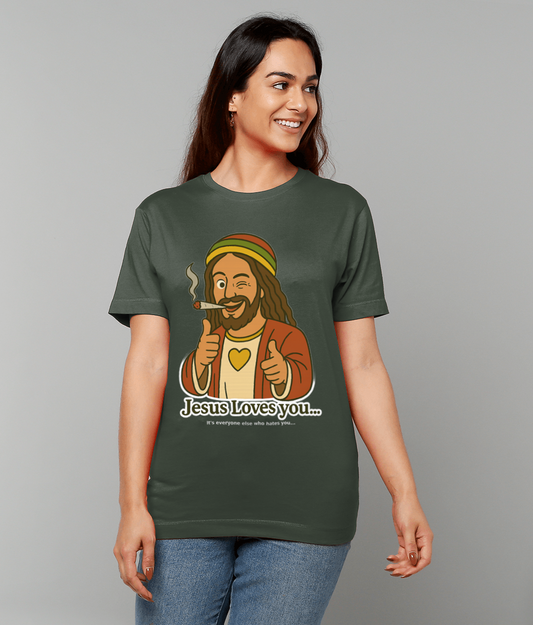 Woman wearing a dark green T-shirt featuring a cartoon Jesus winking, smoking a rolled cigarette and pointing; gray studio background; T-shirt text reads "Jesus Loves you..." "It's everyone else who hates you..."