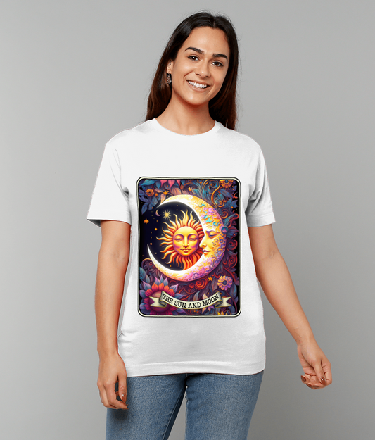 White T-shirt displays colorful sun-and-moon artwork with crescent moon face and radiant sun surrounded by flowers, banner reading "THE SUN AND MOON", worn by smiling person against plain gray backdrop.