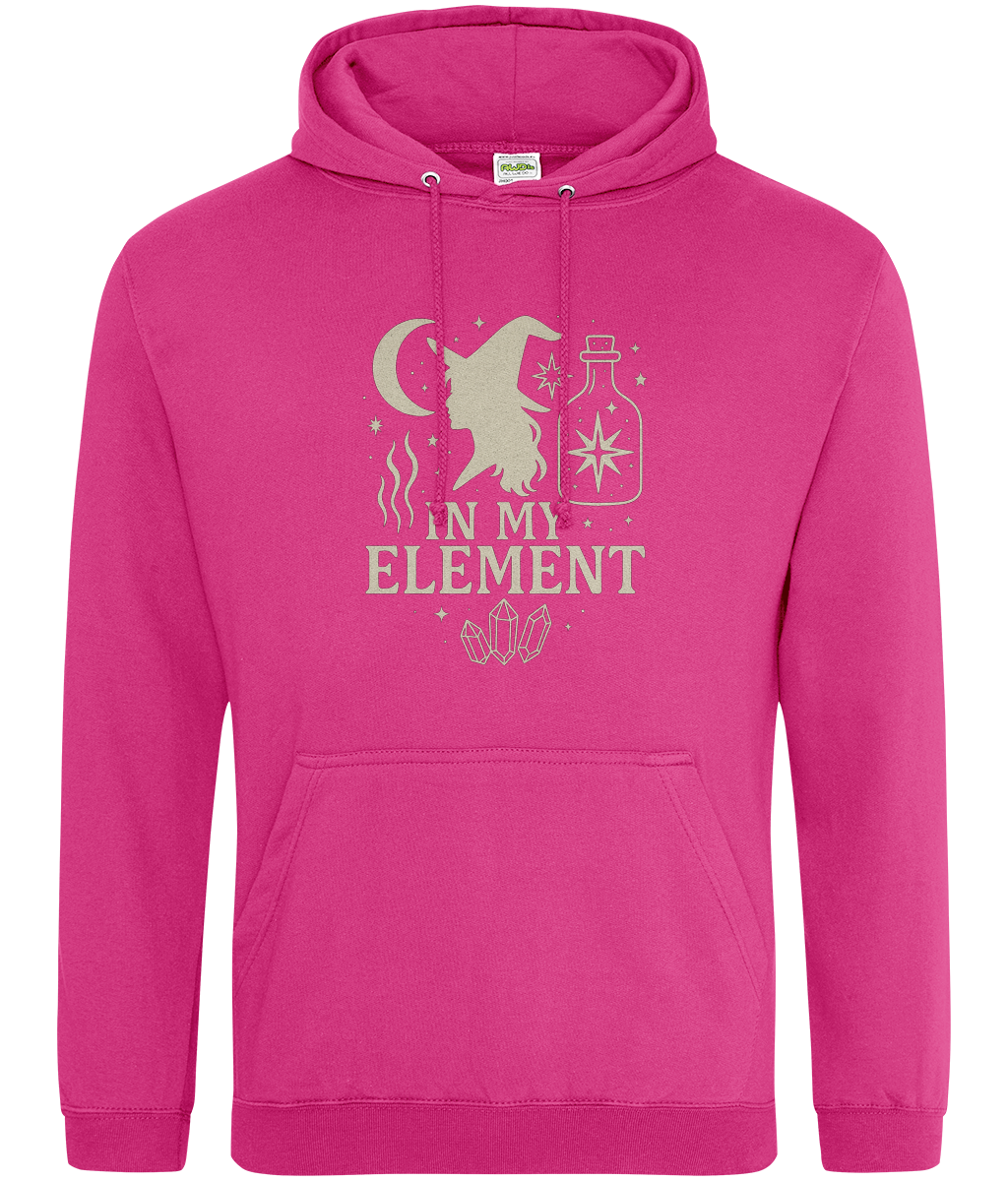 Pink hooded sweatshirt displays a beige witch-silhouette design with crescent moon, stars, potion bottle and crystals and the text "IN MY ELEMENT" centered on a plain white background.