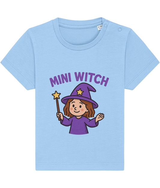 Light blue children's T-shirt features a smiling cartoon mini witch in a purple hat and robe holding a star-tipped wand, printed under purple text reading 'MINI WITCH'.