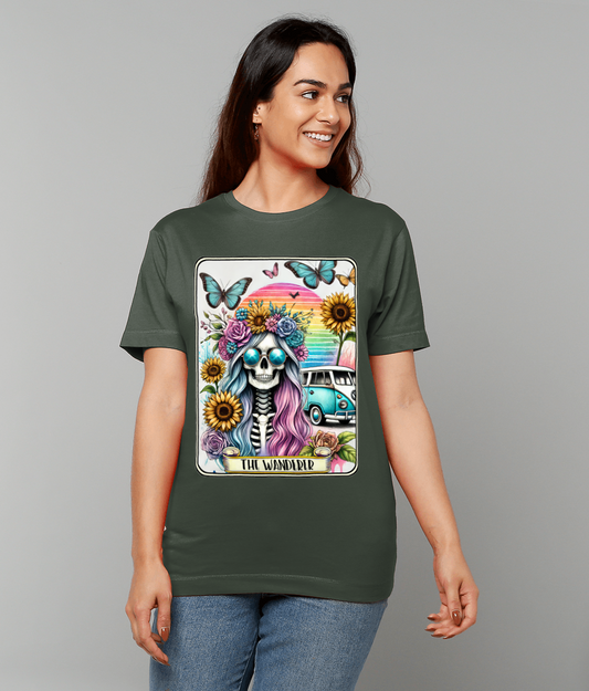 T-shirt displaying a colorful skull with flower crown, sunglasses, sun, butterflies and a teal van labeled "THE WANDERER" is worn by a smiling woman against a plain gray studio background.