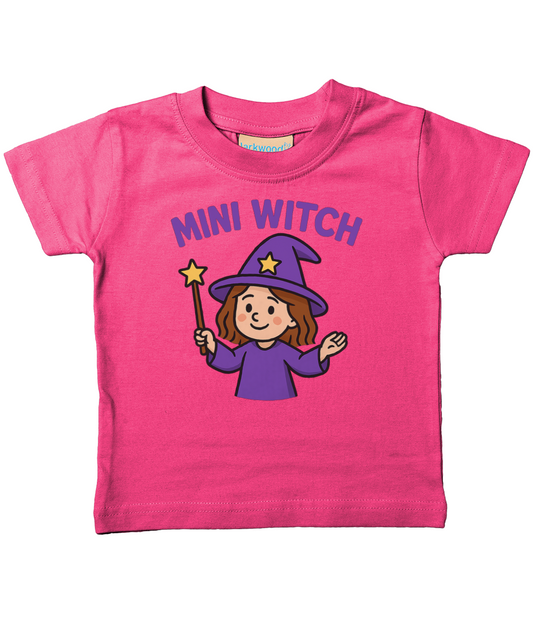 Pink toddler T-shirt reading "MINI WITCH" above a smiling cartoon witch in a purple hat and robe holding a star-tipped wand centered on the shirt.