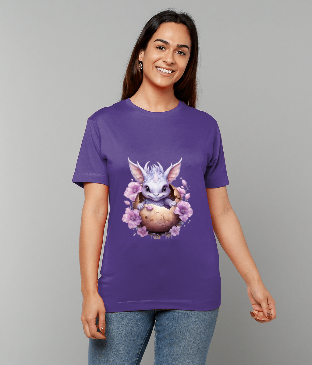 Purple T-shirt featuring a small lavender dragon peeking from a cracked egg surrounded by pink flowers, worn by a smiling woman standing against a plain light gray background.