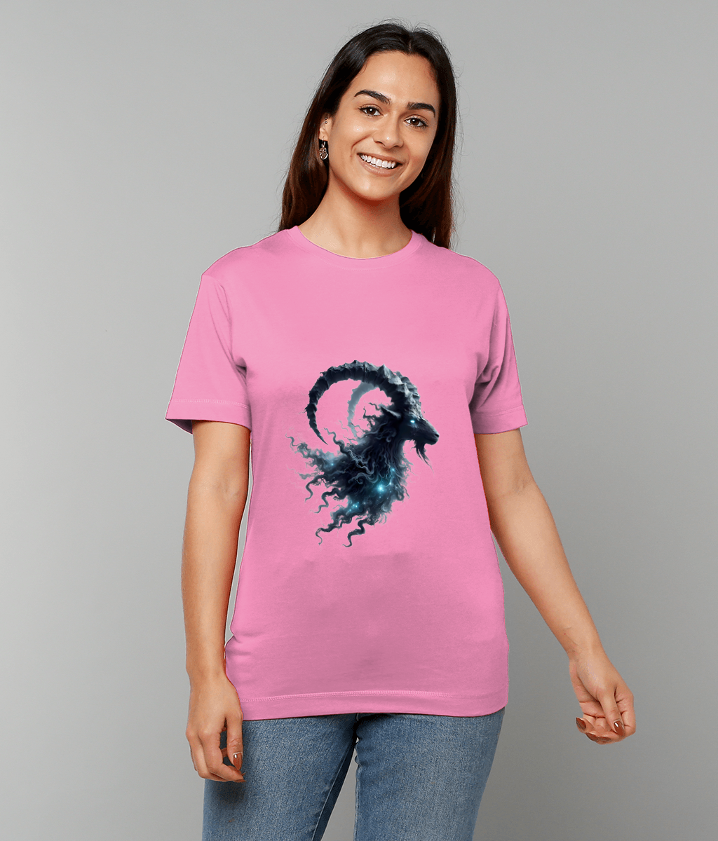Woman wearing a pink t-shirt displays a dark cosmic ram skull graphic while smiling softly and standing against a plain light gray studio background.