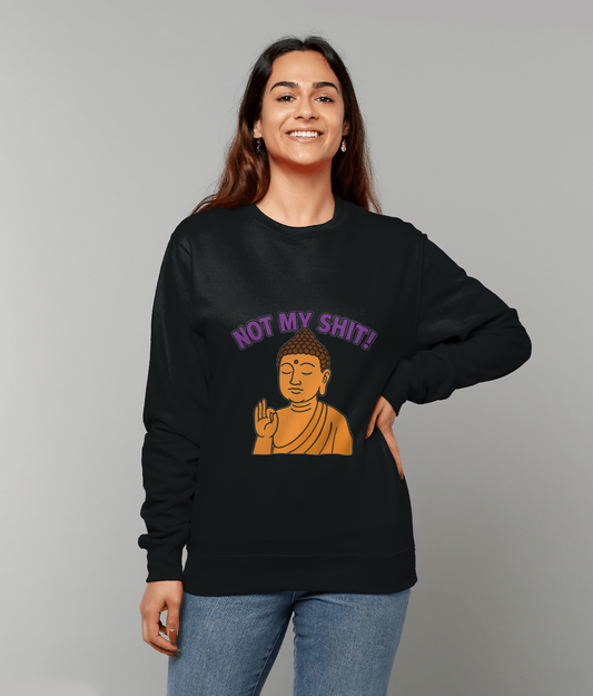Smiling young woman wears a black sweatshirt featuring an orange Buddha raising a hand and purple text reading "NOT MY SHIT!" while standing against a plain gray background with one hand on her hip.