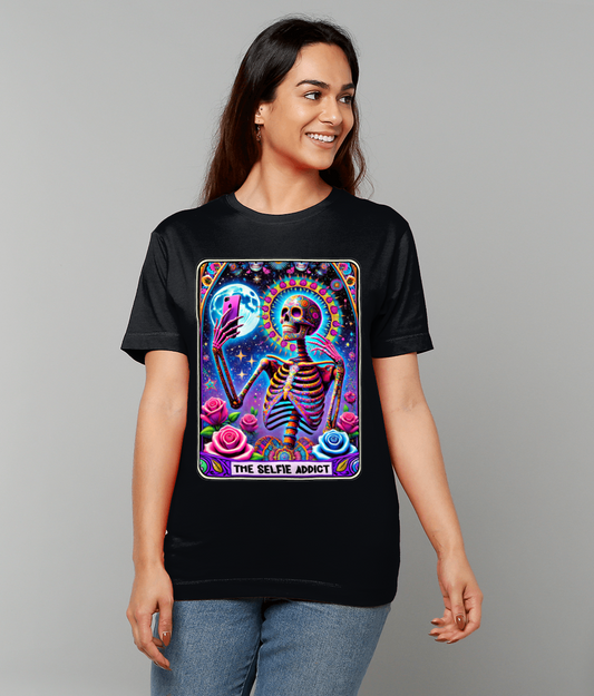 Black t-shirt displaying a vibrant tarot-style illustration of a skeleton taking a selfie, labeled "THE SELFIE ADDICT", worn by a smiling woman against a plain light gray background.