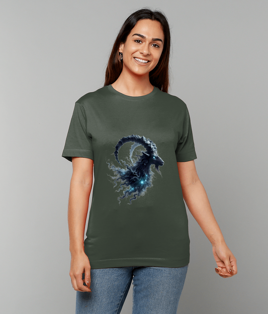 Dark green t-shirt features a swirling blue cosmic ram head with curled horns emitting smoky nebula tendrils worn by a smiling person against a plain gray backdrop.