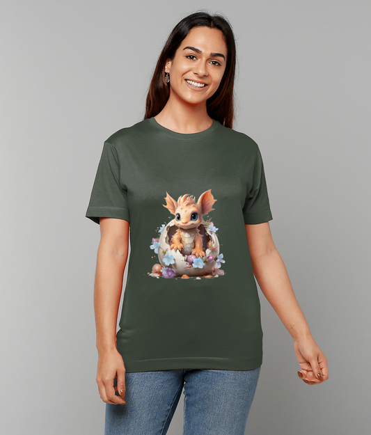 T-shirt displays a chubby baby dragon emerging from a cracked eggshell surrounded by pastel flowers worn by a smiling woman against a plain gray backdrop