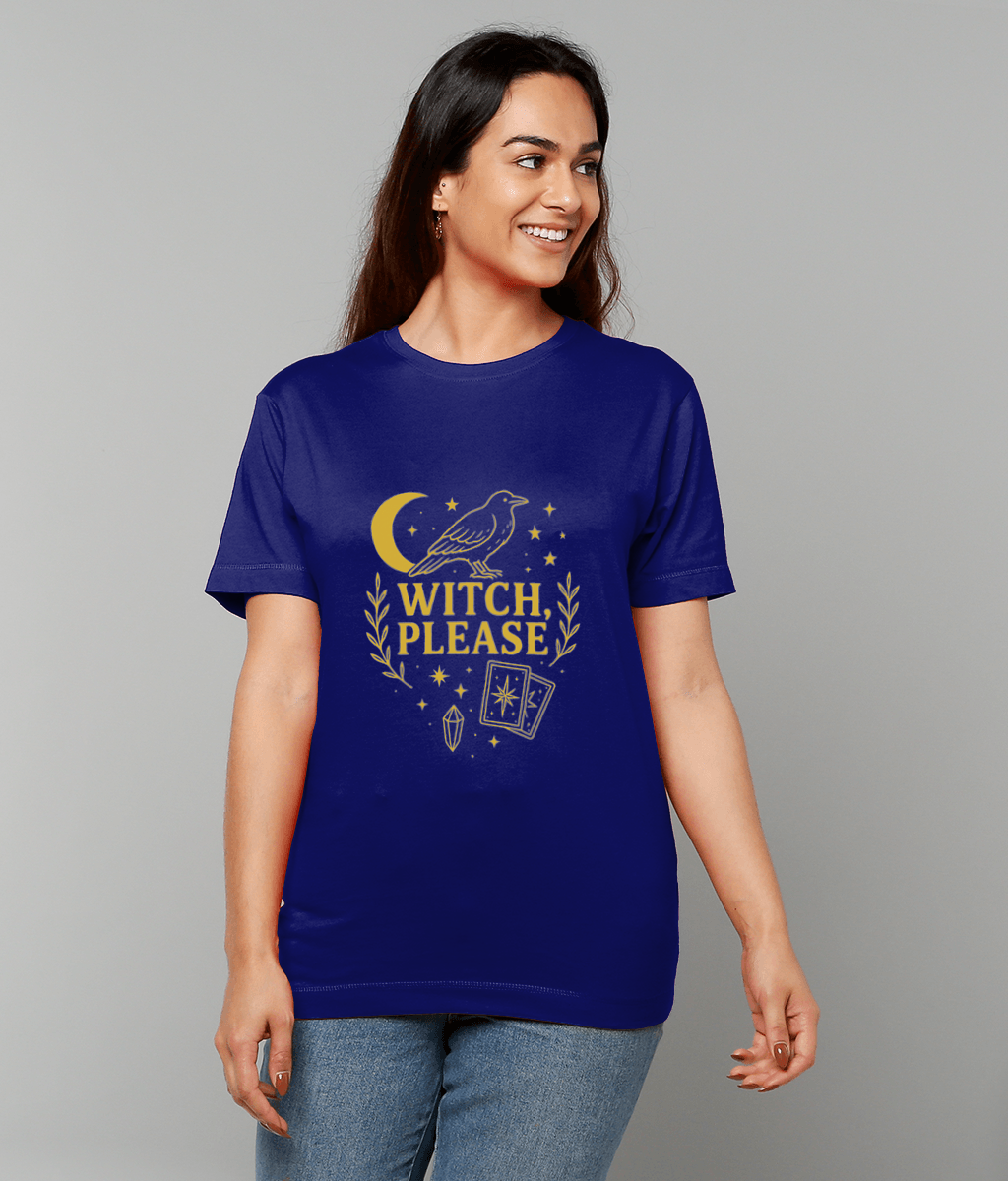 A woman wears a blue T-shirt showing a gold crow above a crescent moon, stars, tarot cards and crystal with the text "WITCH, PLEASE", smiling against a gray background.