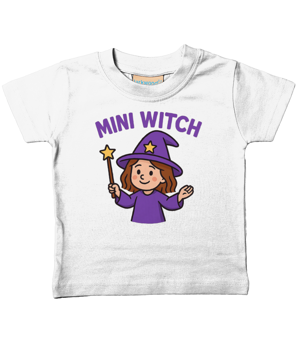 White toddler T-shirt displays text "MINI WITCH" above a smiling girl in a purple witch hat and robe holding a star-tipped wand on a plain white background.
