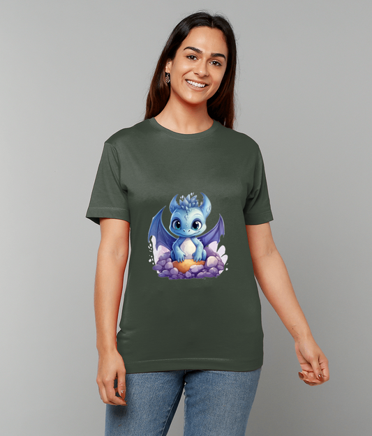 A blue baby dragon sits on purple stones and holds an orange egg printed on an olive-green T-shirt worn by a smiling woman against a plain gray backdrop.