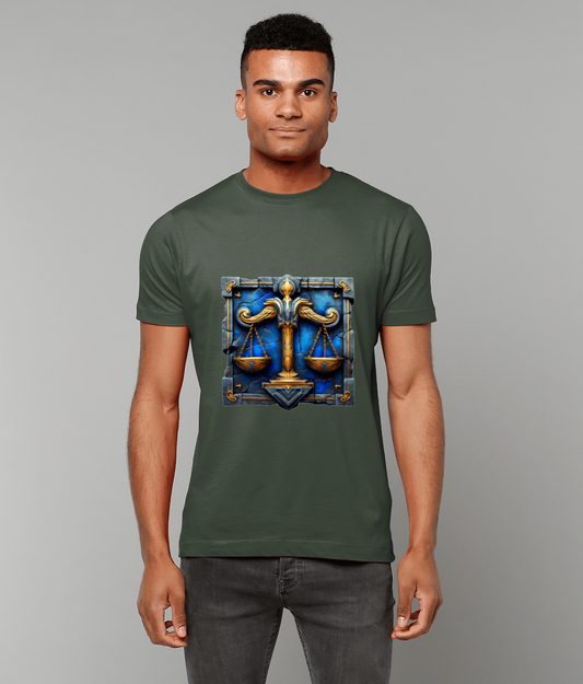 A man wears an olive-green T-shirt that displays ornate golden balance scales set on a blue stone tile while he stands facing forward against a plain light-gray background.