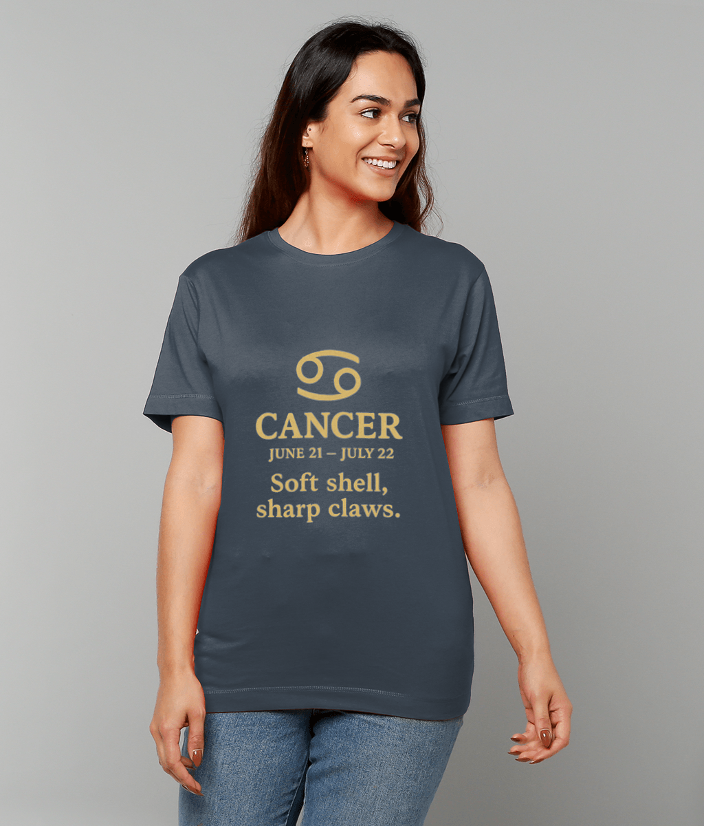 Woman wearing dark gray T-shirt showing Cancer glyph and text 'CANCER JUNE 21 - JULY 22 Soft shell, sharp claws.' She smiles looking right against a plain light gray background.