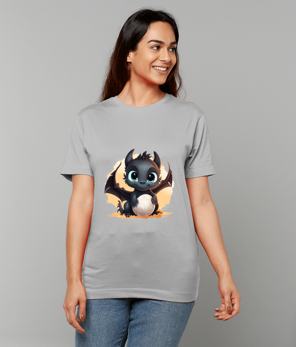 Woman wearing light gray T-shirt featuring a cute black baby dragon clutching a white egg with tiny wings, she smiles and stands before a plain gray studio background.